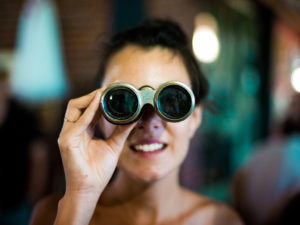 1 woman, with binoculars looking at camera